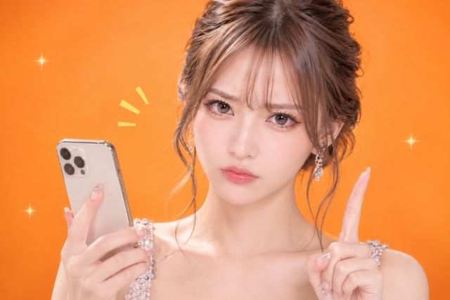 スマホを持って真剣な表情でお人差し指を立てる女性