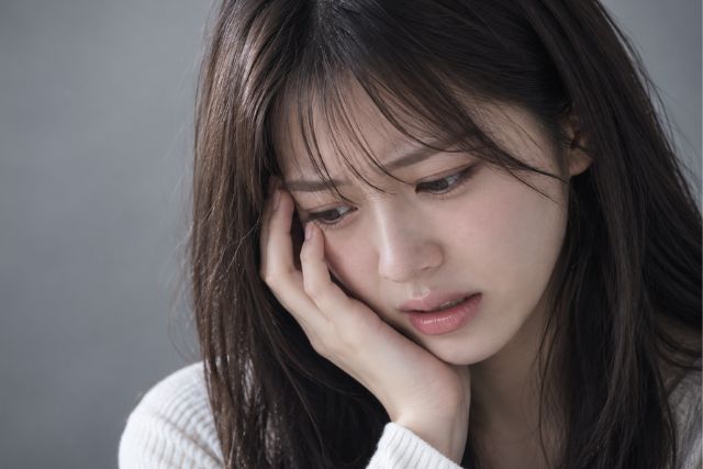 顔に手を当てる辛そうな女性