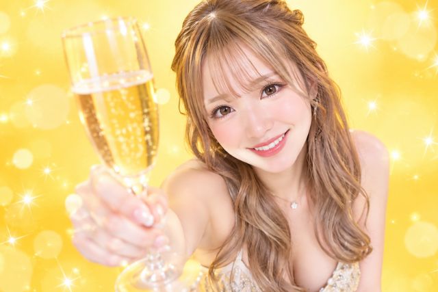 シャンパングラスをカメラの方に向けて掲げて笑顔の女性