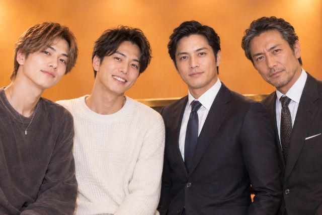 男性が四人並んでいる。左二人は私服で右二人はスーツ。