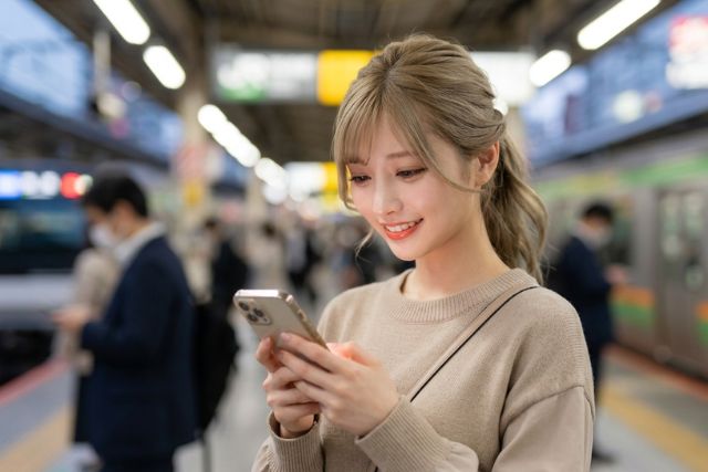 駅でスマホを触る若い女性
