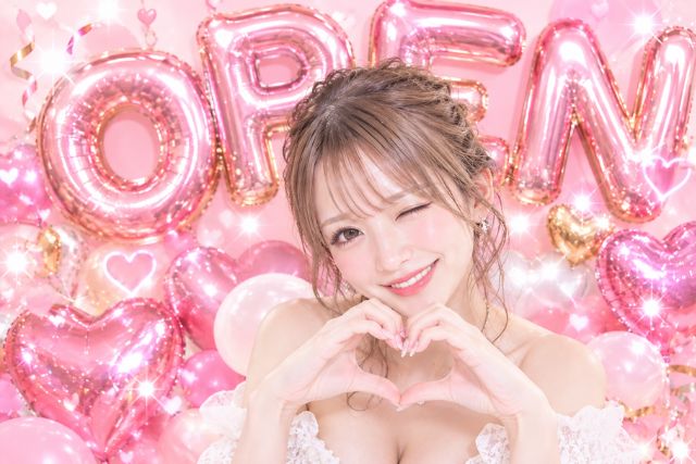 シャンパングラスを両手に持って笑顔の女の子。後ろにはバルーンの装飾がある。ハートのバルーンや丸いバルーン