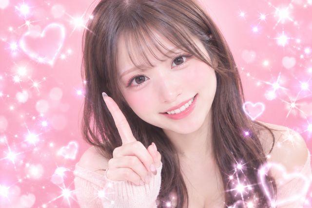 髪の毛を下ろしてちょっと暗めの髪色の女の子。童顔でかわいらしい系。人差し指を立てて笑顔でこちらを向いている