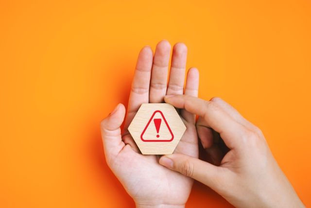 オレンジの背景の前でビックリマークを乗せる女性の手