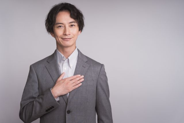 胸を押さえるグレーのスーツを着たビジネスマン