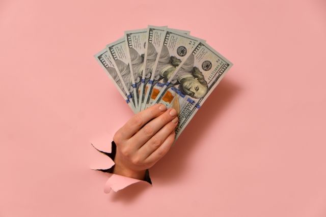 ピンクの背景から出すお札を持った女性の手