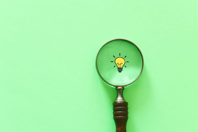 緑の背景の前にある虫眼鏡と電球マーク